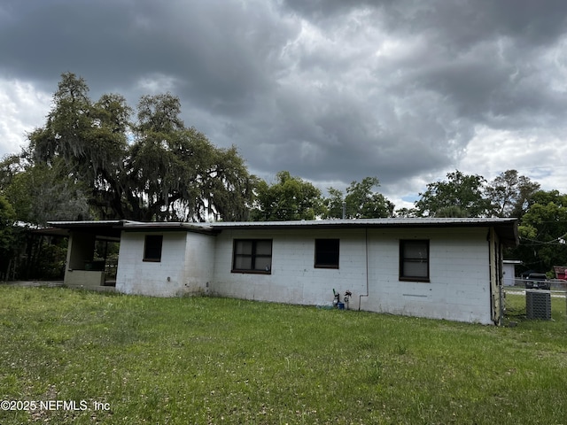rear view of property featuring a yard, metal roof, and concrete block siding