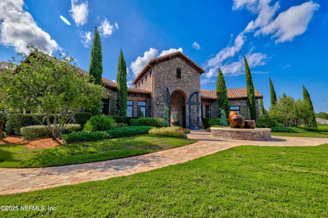 mediterranean / spanish-style house with a tiled roof, a front yard, and stone siding