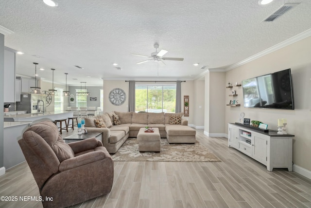 living room with a ceiling fan, crown molding, light wood finished floors, and visible vents