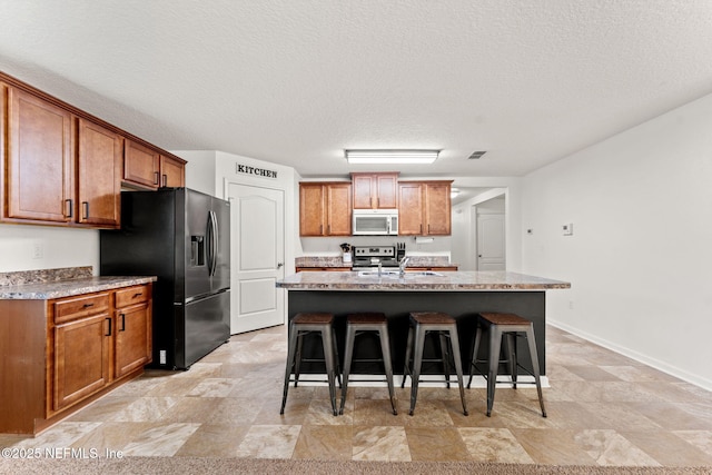 9087 Leicestershire Ct, Jacksonville, FL 32219 - kitchen with a kitchen bar, brown cabinets, a center island with sink, a sink, and black fridge