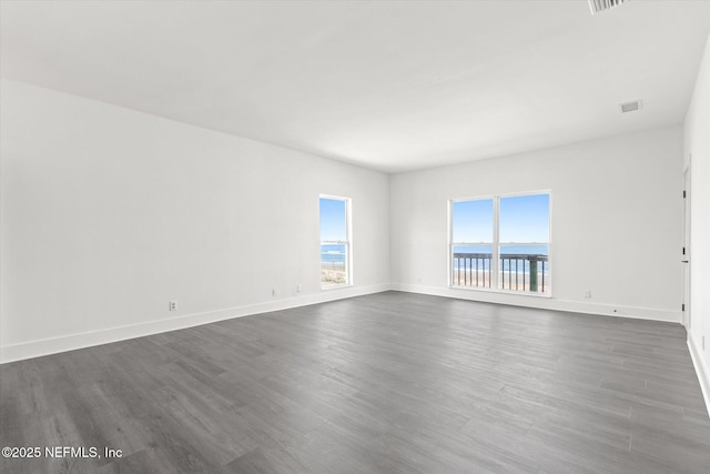empty room featuring baseboards, dark wood-style floors, and visible vents
