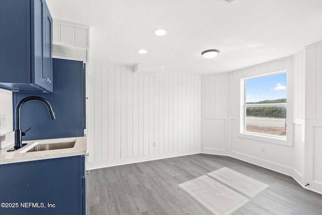 kitchen with light countertops, blue cabinets, light wood finished floors, and a sink