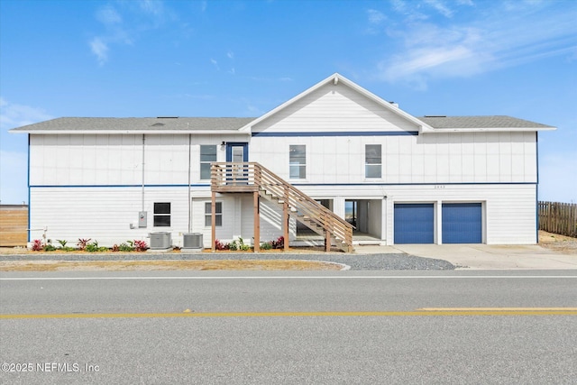 view of front facade with an attached garage, driveway, central AC unit, and stairs