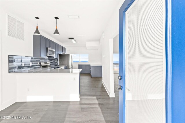 kitchen featuring a peninsula, visible vents, wood finished floors, stainless steel appliances, and backsplash