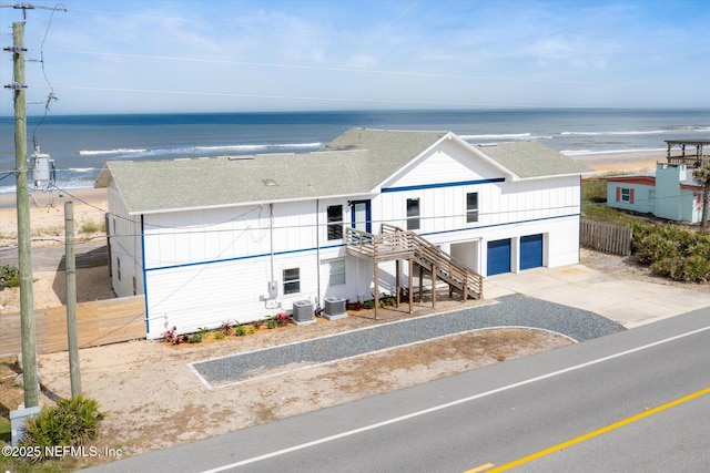 view of front of house with central air condition unit, driveway, an attached garage, stairs, and a shingled roof