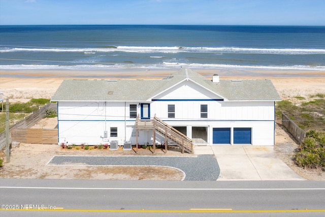 view of front of property with concrete driveway, stairway, a beach view, a water view, and fence