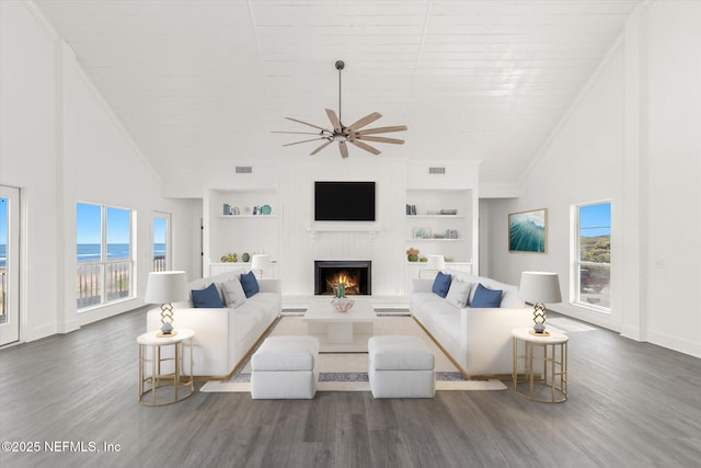 living area with built in features, a wealth of natural light, ceiling fan, and a lit fireplace
