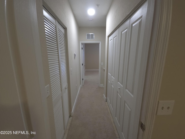 corridor featuring light carpet, visible vents, and baseboards