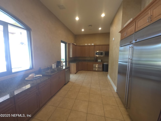 kitchen featuring dark stone countertops, light tile patterned floors, built in appliances, a sink, and recessed lighting