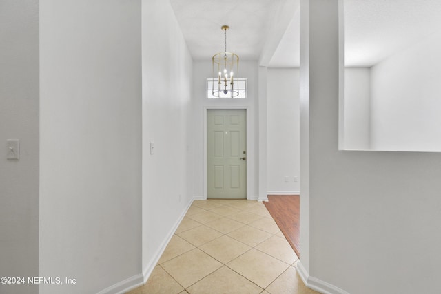 corridor with light tile patterned flooring, baseboards, and a chandelier