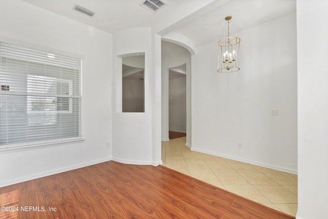 empty room with arched walkways, visible vents, a chandelier, and tile patterned flooring