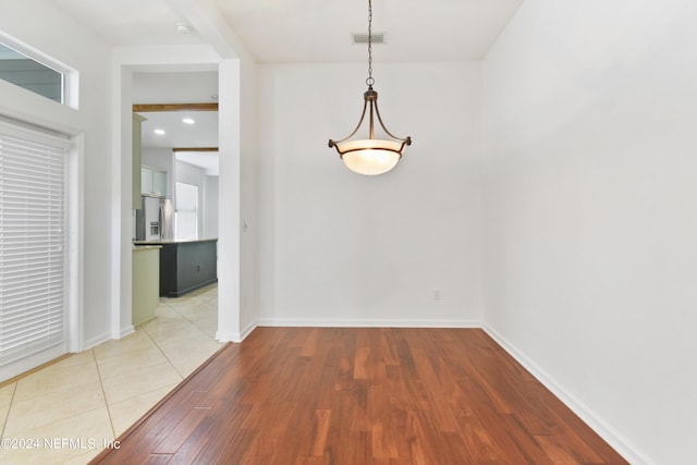 unfurnished dining area featuring light wood finished floors, baseboards, visible vents, and beamed ceiling