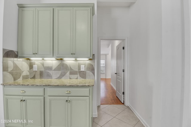 kitchen with light tile patterned flooring, green cabinetry, light stone counters, tasteful backsplash, and baseboards