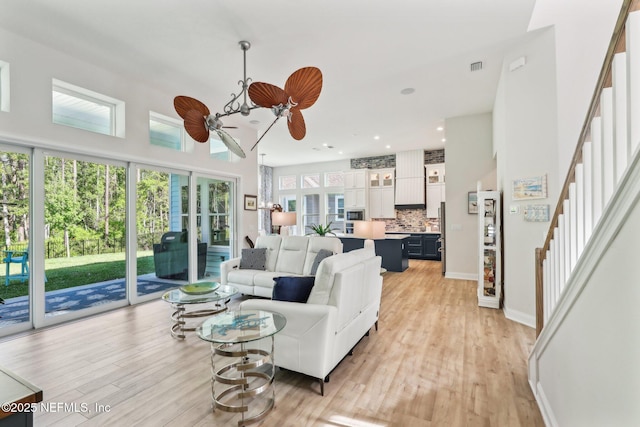 living room with ceiling fan, light wood-type flooring, visible vents, stairs, and baseboards