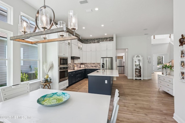 kitchen featuring light countertops, light wood-style floors, white cabinetry, stainless steel appliances, and backsplash