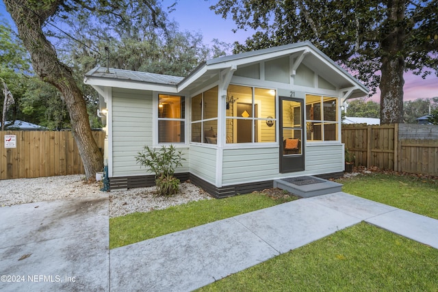 bungalow with a yard, a sunroom, fence, and metal roof