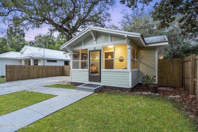 bungalow featuring metal roof, a front yard, a sunroom, and fence