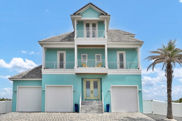 view of front of house featuring a balcony, fence, decorative driveway, stucco siding, and french doors