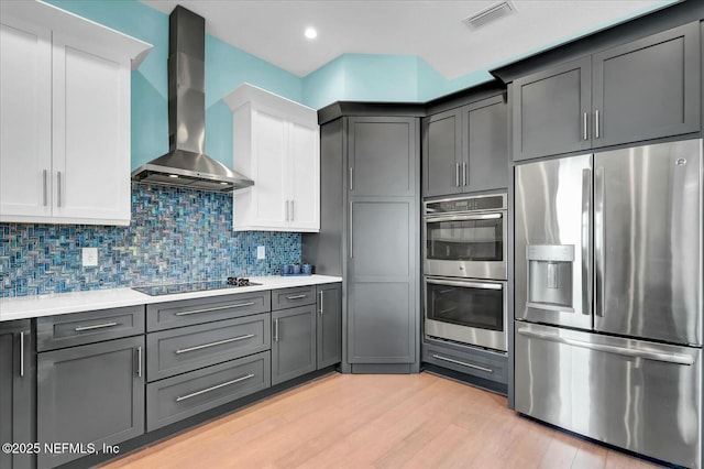 kitchen with light countertops, visible vents, light wood-style flooring, stainless steel appliances, and wall chimney range hood