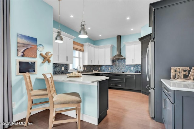 kitchen with white cabinetry, a breakfast bar area, backsplash, a peninsula, and wall chimney exhaust hood