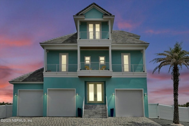 view of front of home featuring driveway, french doors, stucco siding, fence, and a balcony