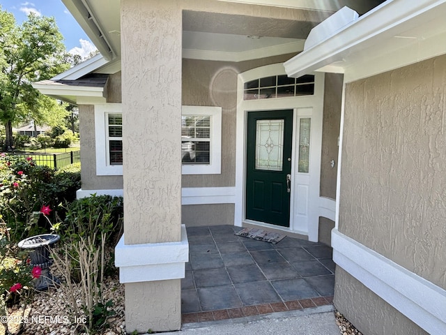 entrance to property with fence, covered porch, and stucco siding