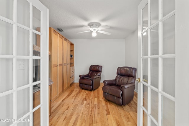 living area with light wood finished floors, french doors, a textured ceiling, and a ceiling fan