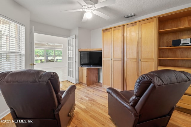 living room with light wood-style floors, visible vents, a textured ceiling, and ceiling fan