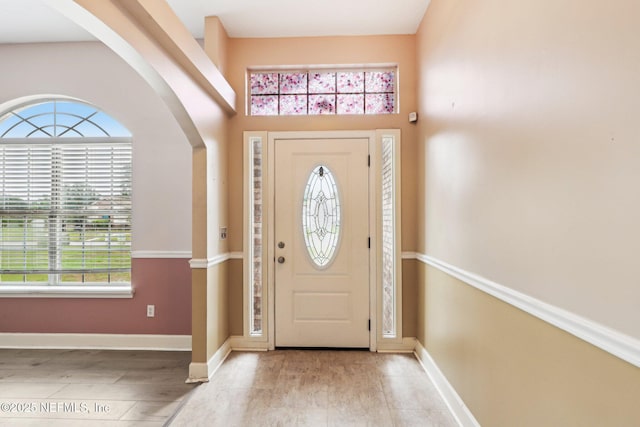 entrance foyer with wood finished floors, arched walkways, and baseboards