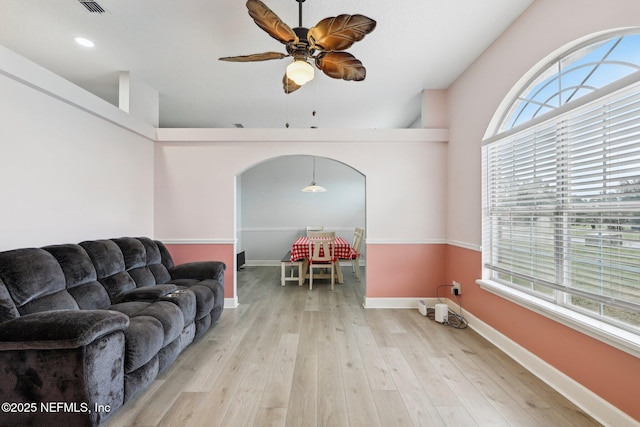 living area with a ceiling fan, wood finished floors, baseboards, and arched walkways
