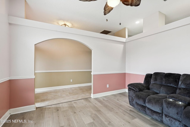living area featuring arched walkways, wood finished floors, a ceiling fan, baseboards, and vaulted ceiling