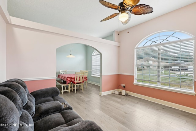 living area with arched walkways, wood finished floors, baseboards, and a ceiling fan