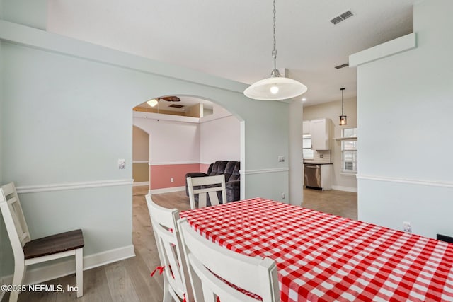 dining space with arched walkways, light wood-style floors, and baseboards