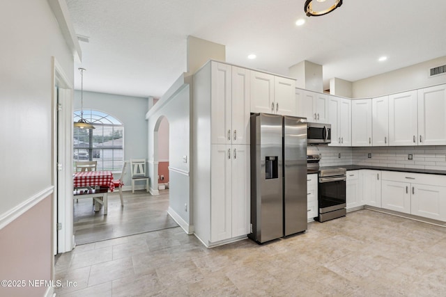kitchen featuring appliances with stainless steel finishes, backsplash, white cabinets, arched walkways, and recessed lighting