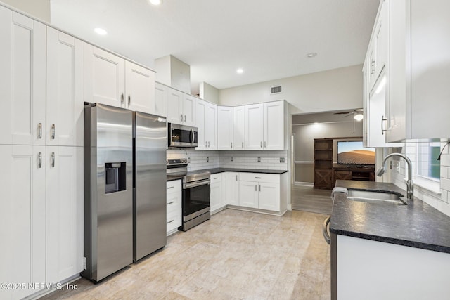 kitchen featuring appliances with stainless steel finishes, a sink, dark countertops, white cabinets, and a ceiling fan