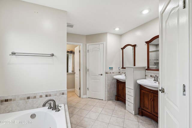 bathroom with two vanities, tile patterned floors, a bath, tile walls, and recessed lighting
