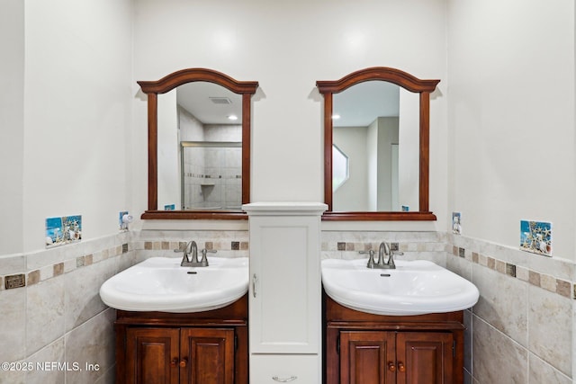 full bath with tile walls, a stall shower, two vanities, and wainscoting