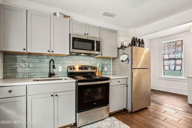 kitchen with visible vents, light countertops, a sink, stainless steel appliances, and dark wood-style floors