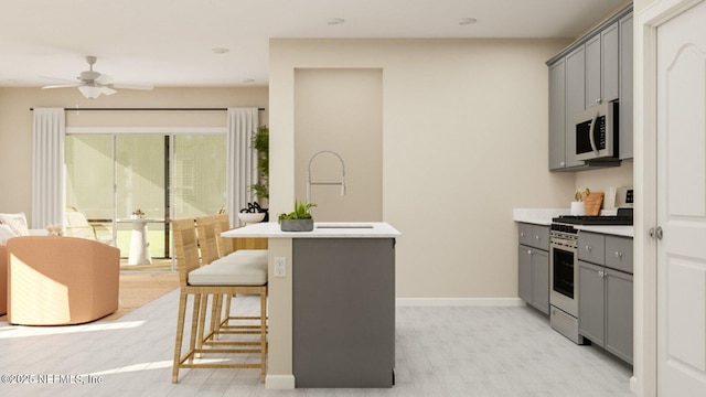 kitchen with light countertops, a breakfast bar area, gray cabinetry, stainless steel gas range, and white microwave