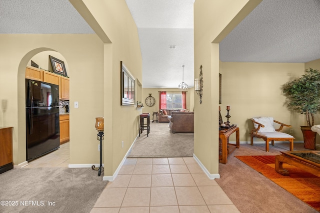 hall featuring light tile patterned floors, a textured ceiling, light carpet, and baseboards