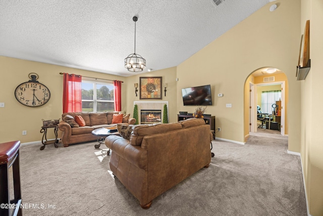 living area featuring carpet flooring, a tiled fireplace, a chandelier, arched walkways, and a textured ceiling