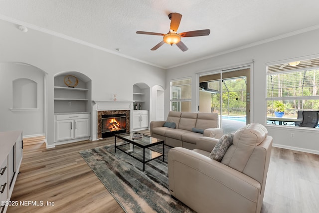 living room with built in shelves, baseboards, light wood-type flooring, a ceiling fan, and a textured ceiling