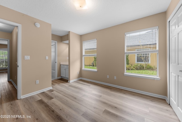 unfurnished bedroom featuring light wood-style flooring, baseboards, and a textured ceiling