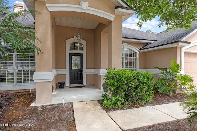 entrance to property featuring a garage, roof with shingles, and stucco siding