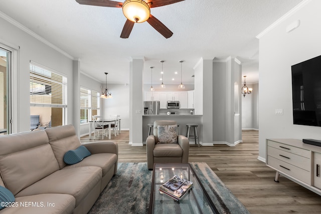 living room featuring ceiling fan with notable chandelier, wood finished floors, baseboards, and ornamental molding