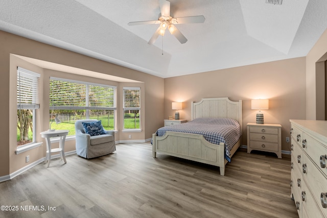 bedroom featuring light wood-style floors, baseboards, visible vents, and a raised ceiling