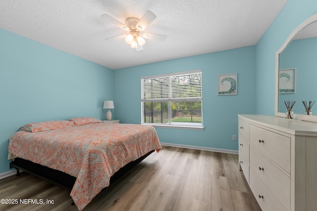 bedroom with baseboards, a ceiling fan, light wood-style floors, and a textured ceiling