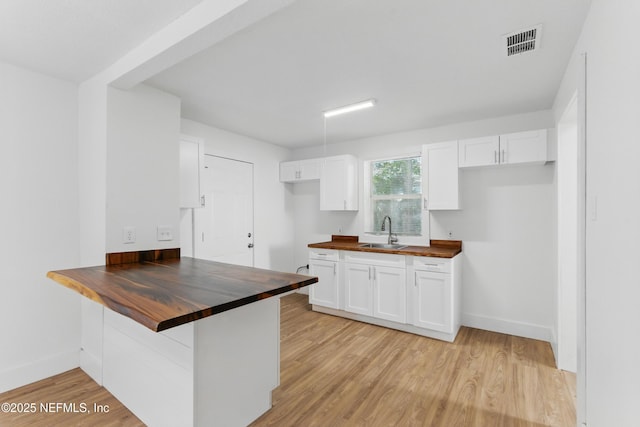 1539 7th St W, Jacksonville, FL 32209 - kitchen featuring a peninsula, light wood finished floors, wooden counters, white cabinetry, and a sink