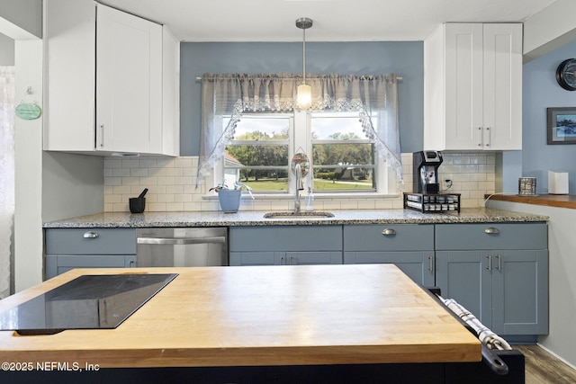 kitchen featuring stainless steel dishwasher, white cabinetry, a sink, and backsplash