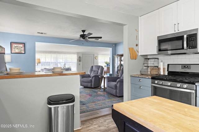 kitchen featuring open floor plan, white cabinets, light wood-style floors, decorative backsplash, and stainless steel appliances